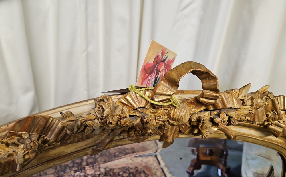 An antique French Louis XVI style giltwood mirror with an arched top, floral garland moulding, and ribbon cresting. View IV