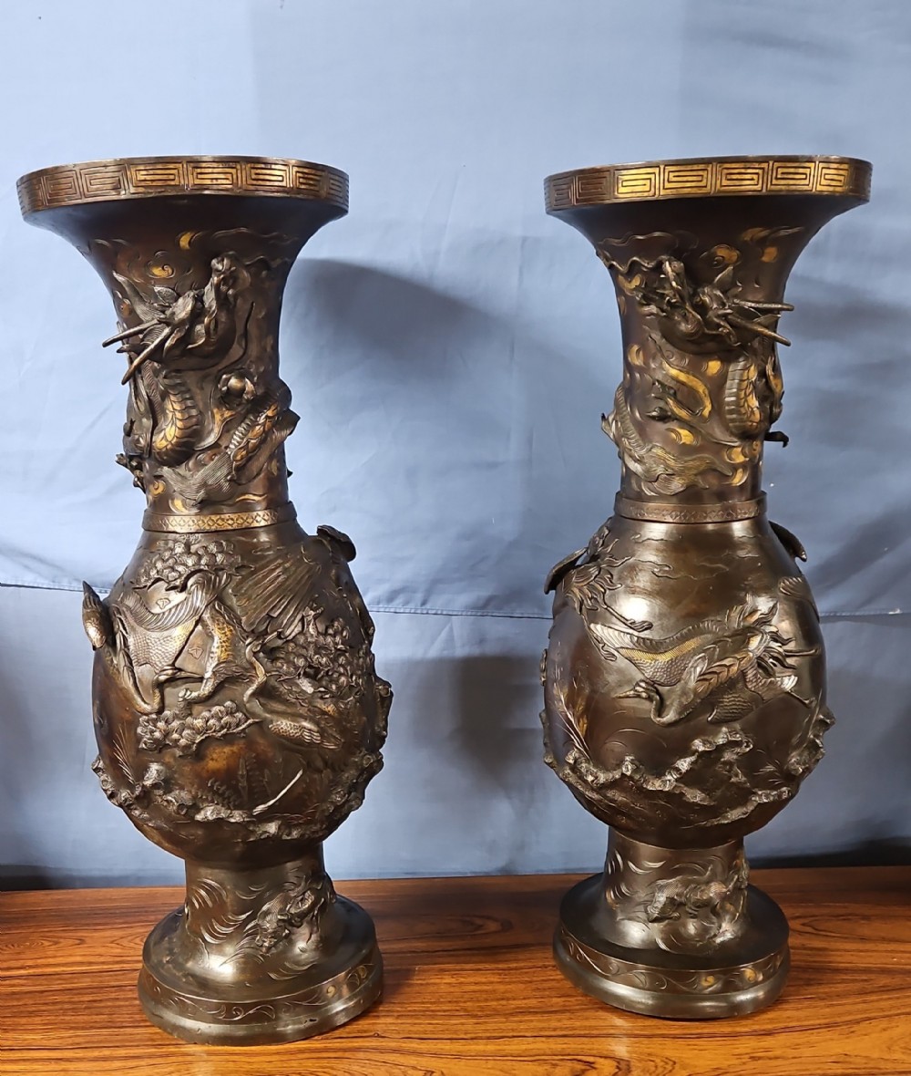 A pair of large Japanese bronze vases featuring high-relief sculpted dragons around the necks and crane motifs on bulbous bases with gilt detailing.