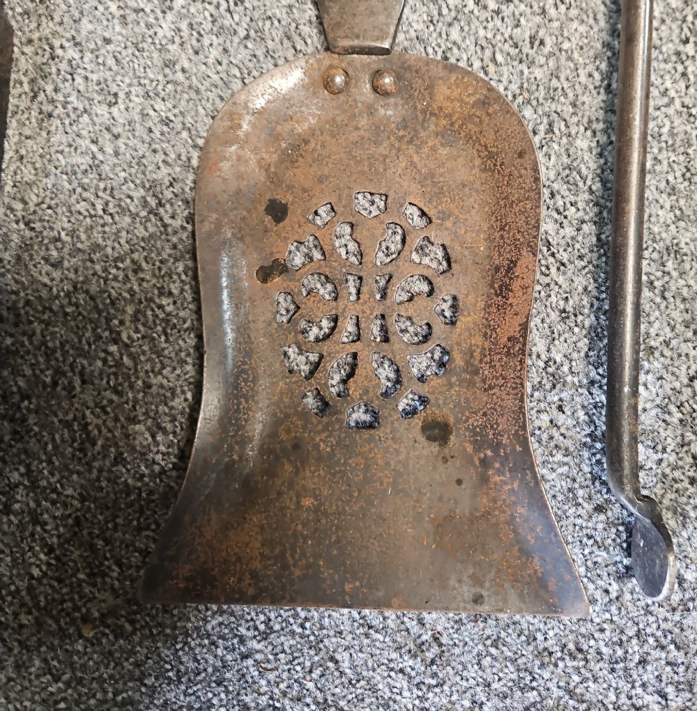 A three-piece set of Georgian polished steel fire tools comprising a poker, a pierced shovel, and a pair of tongs with faceted finials. View V