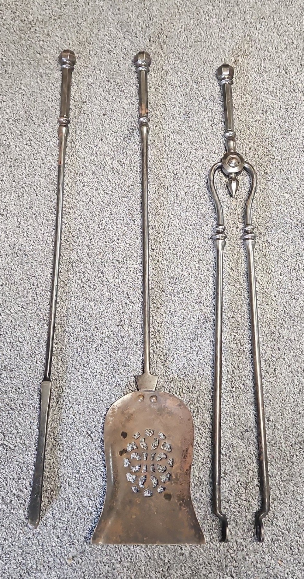 A three-piece set of Georgian polished steel fire tools comprising a poker, a pierced shovel, and a pair of tongs with faceted finials. View VI