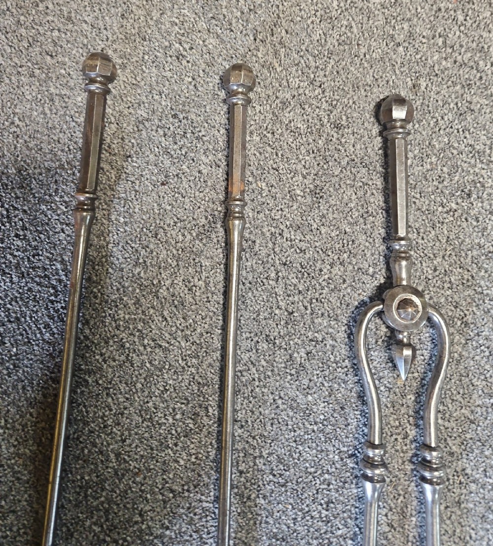 A three-piece set of Georgian polished steel fire tools comprising a poker, a pierced shovel, and a pair of tongs with faceted finials. View VII