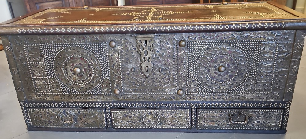 A mid-Victorian wooden Zanzibar chest decorated with intricate brass studs, geometric brass sheeting, and three base drawers. View IV