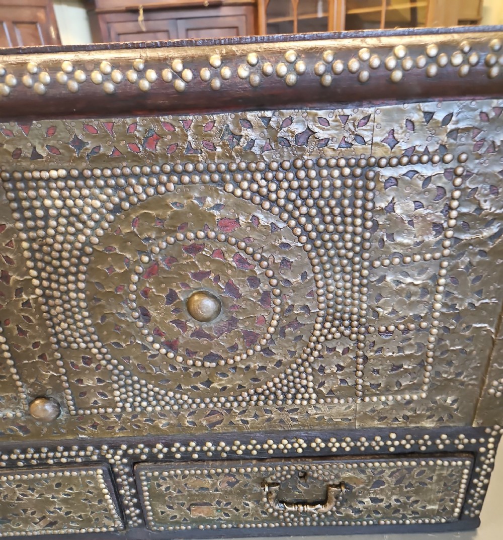 A mid-Victorian wooden Zanzibar chest decorated with intricate brass studs, geometric brass sheeting, and three base drawers. View V