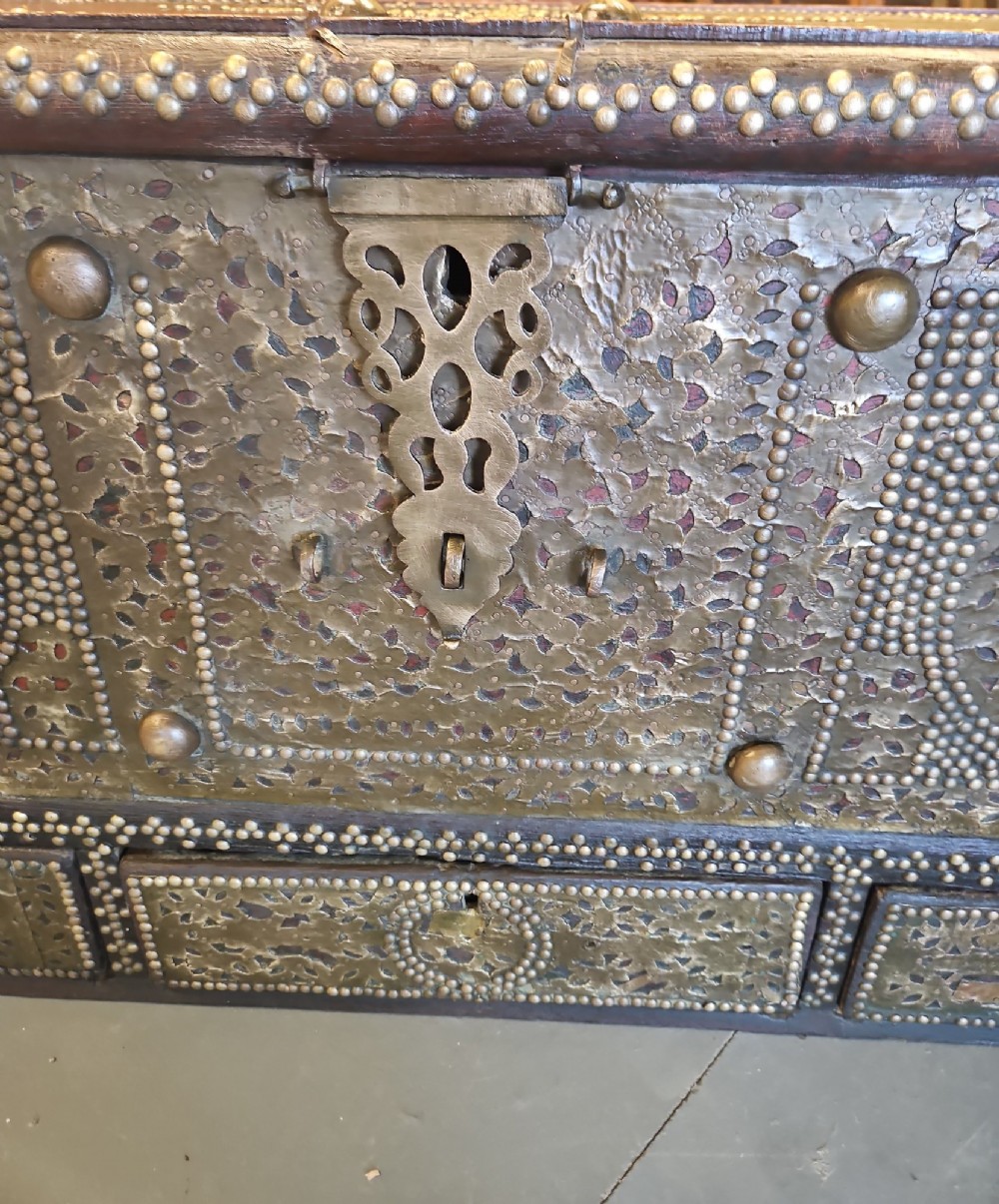 A mid-Victorian wooden Zanzibar chest decorated with intricate brass studs, geometric brass sheeting, and three base drawers. View VI