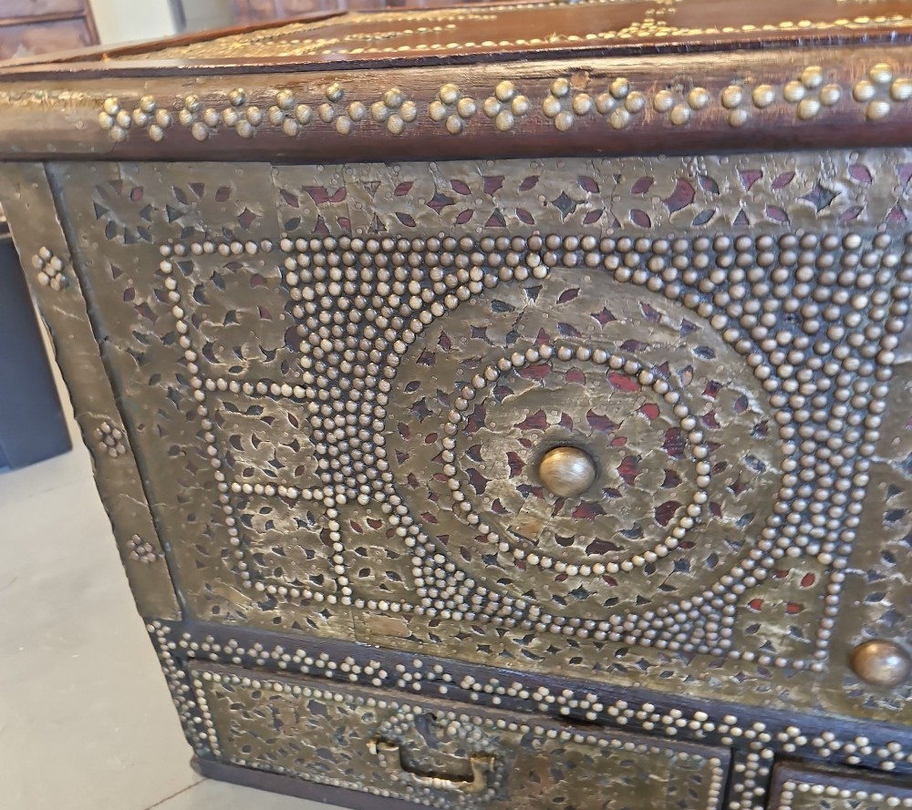 A mid-Victorian wooden Zanzibar chest decorated with intricate brass studs, geometric brass sheeting, and three base drawers. View VII