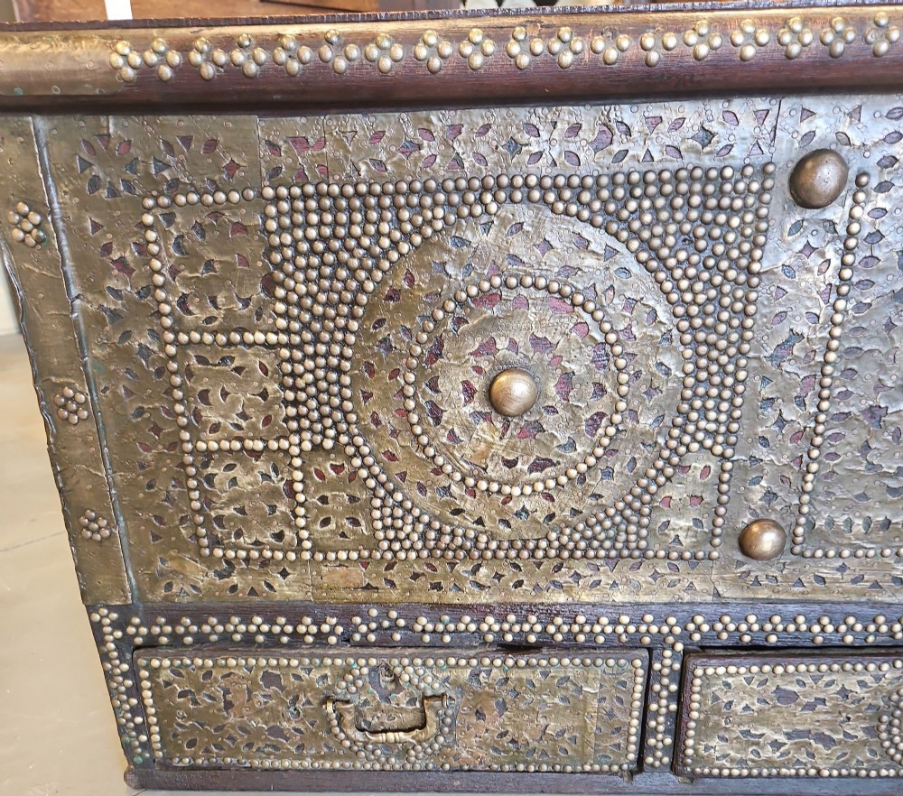 A mid-Victorian wooden Zanzibar chest decorated with intricate brass studs, geometric brass sheeting, and three base drawers. View VIII