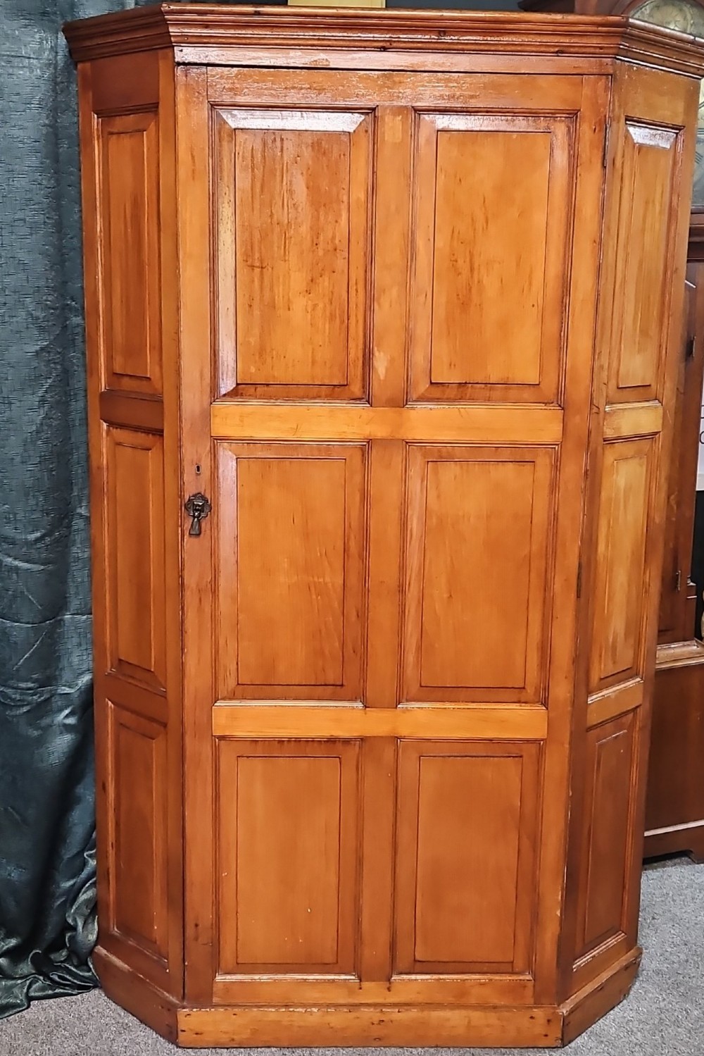 A tall Victorian pine corner wardrobe with fielded panel doors, a brass escutcheon, and a moulded cornice.