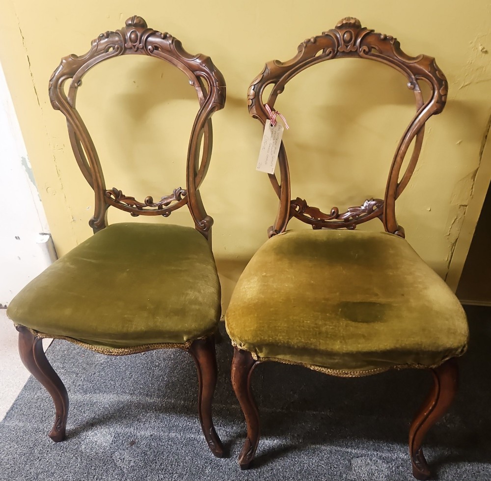A pair of Victorian carved walnut balloon-back side chairs featuring olive green velvet upholstered seats and front cabriole legs.