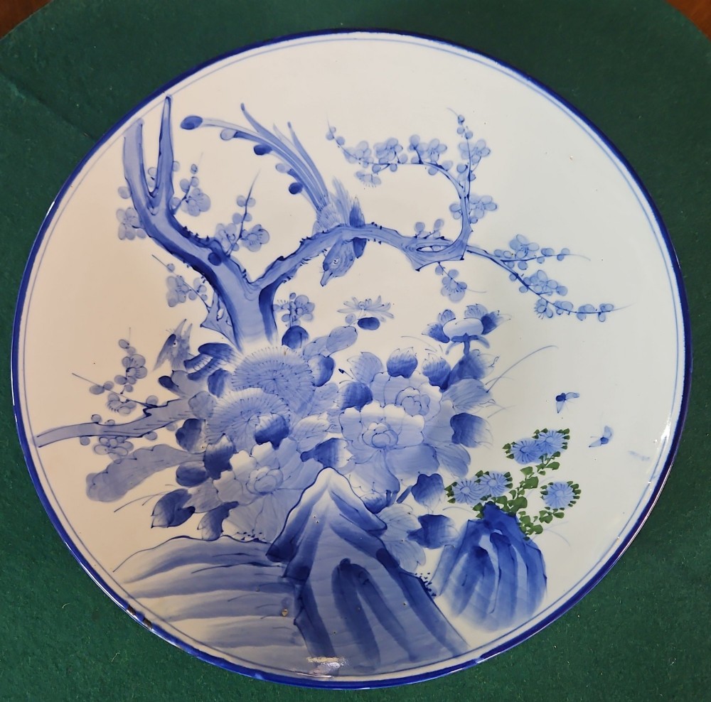 A circular blue and white Japanese Arita porcelain charger decorated with a flowering prunus branch and chrysanthemum blossoms.