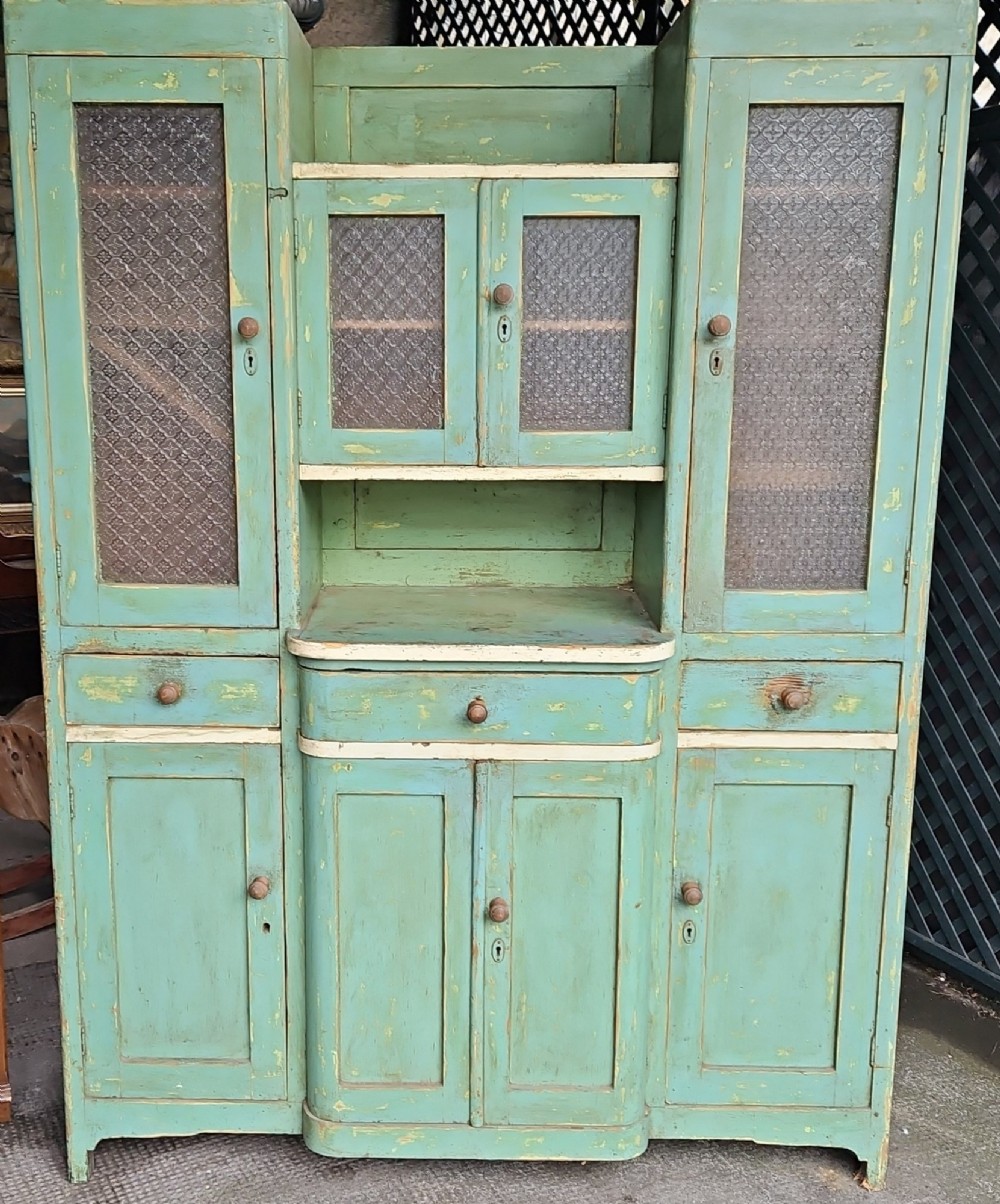 A distressed green painted pine kitchen cabinet featuring upper glazed doors, drawers, and lower panelled wooden doors.