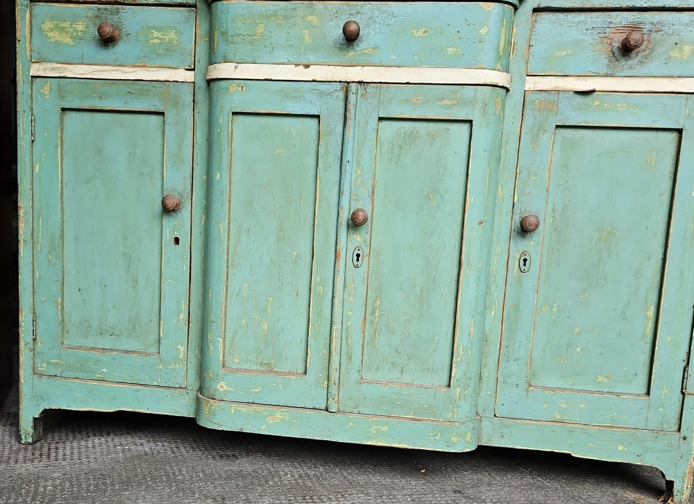 A distressed green painted pine kitchen cabinet featuring upper glazed doors, drawers, and lower panelled wooden doors. View V