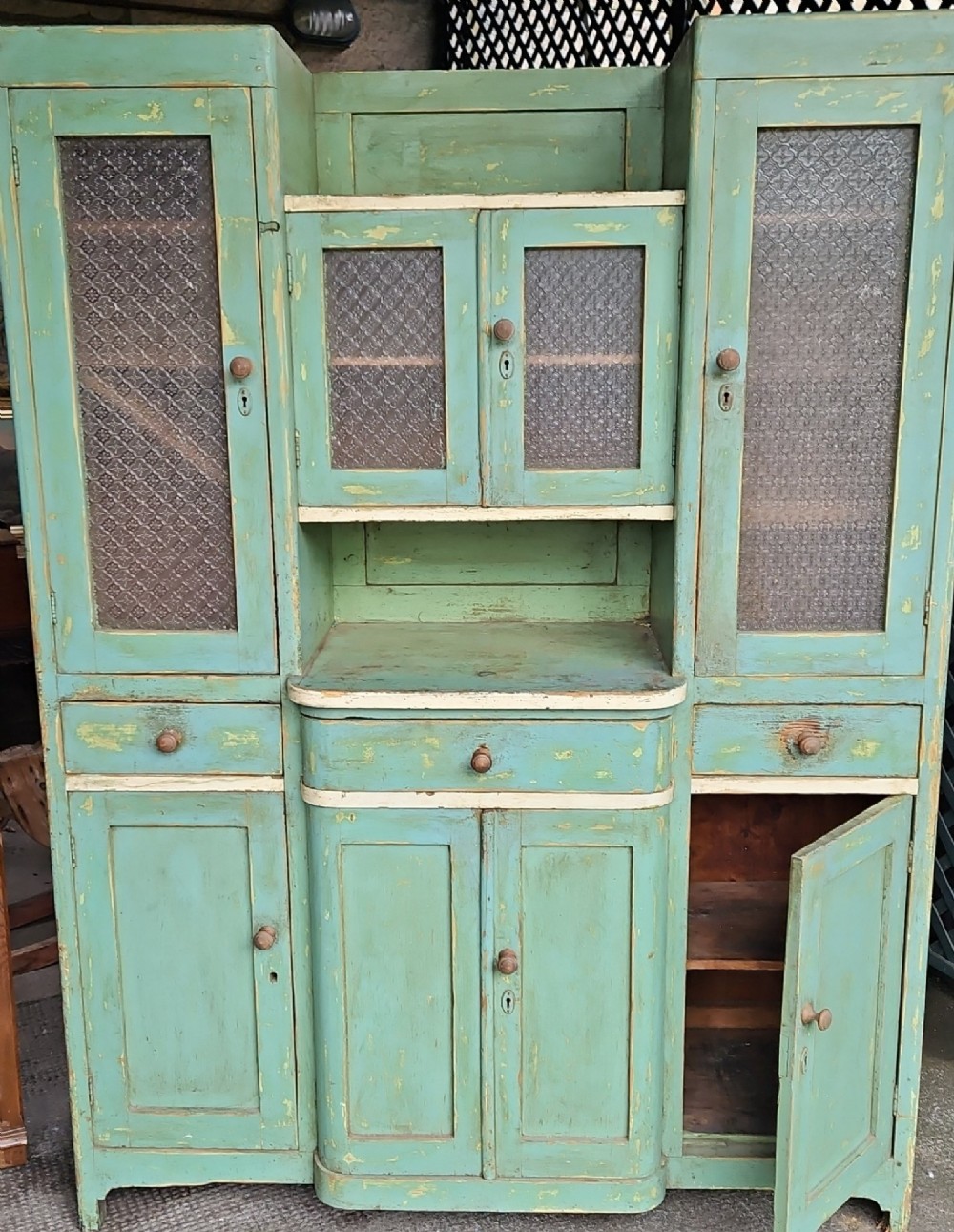 A distressed green painted pine kitchen cabinet featuring upper glazed doors, drawers, and lower panelled wooden doors. View IX