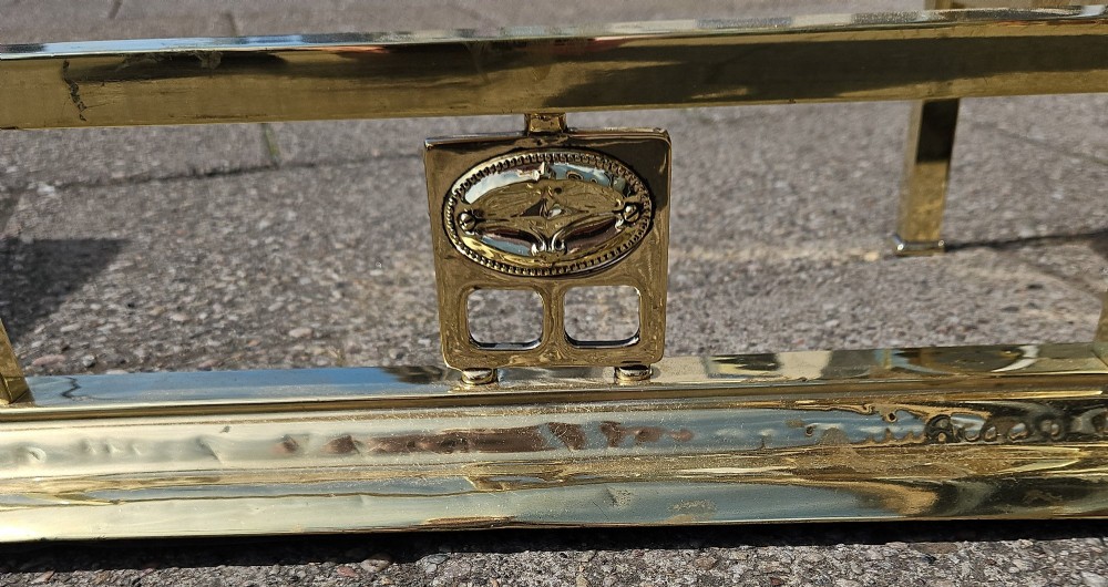 A Victorian brass club fender featuring a polished metal frame with upright supports and two red leather buttoned seats. View V