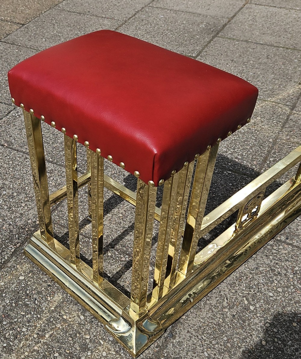 A Victorian brass club fender featuring a polished metal frame with upright supports and two red leather buttoned seats. View VI