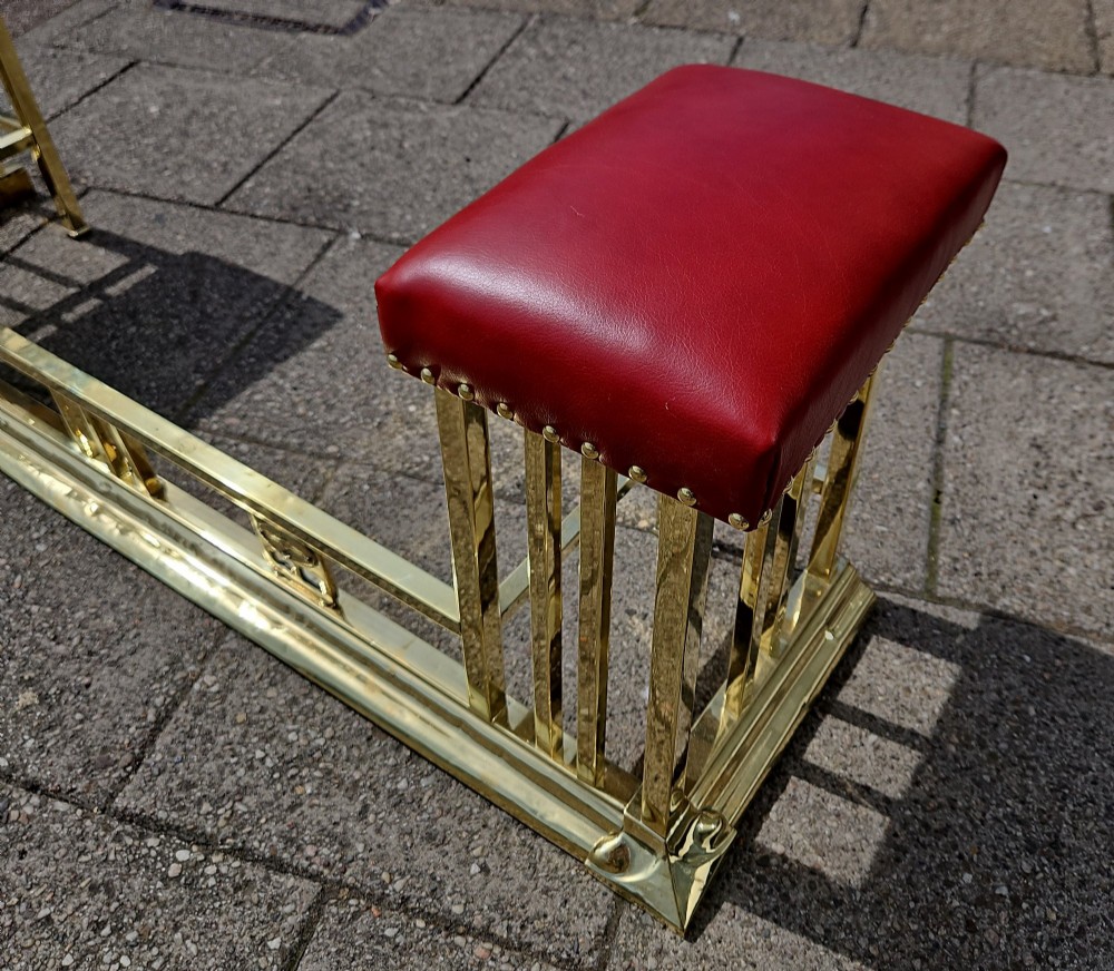 A Victorian brass club fender featuring a polished metal frame with upright supports and two red leather buttoned seats. View VII