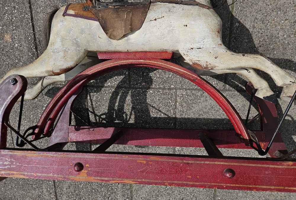 An antique carved wooden rocking horse with a grey painted finish, dark leather saddle, and black horsehair mane, mounted on a dark red glider stand. View IV