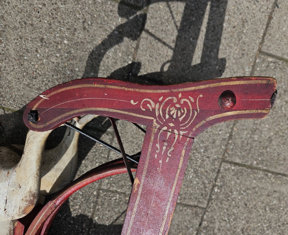 An antique carved wooden rocking horse with a grey painted finish, dark leather saddle, and black horsehair mane, mounted on a dark red glider stand. View V