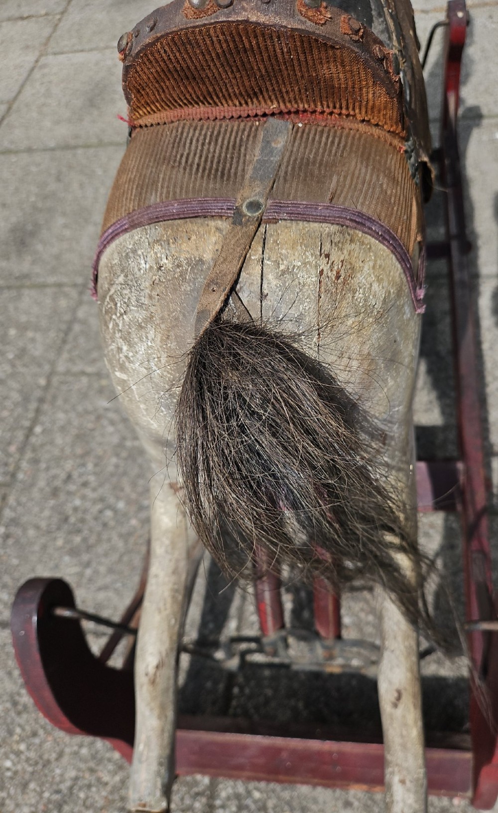 An antique carved wooden rocking horse with a grey painted finish, dark leather saddle, and black horsehair mane, mounted on a dark red glider stand. View VIII