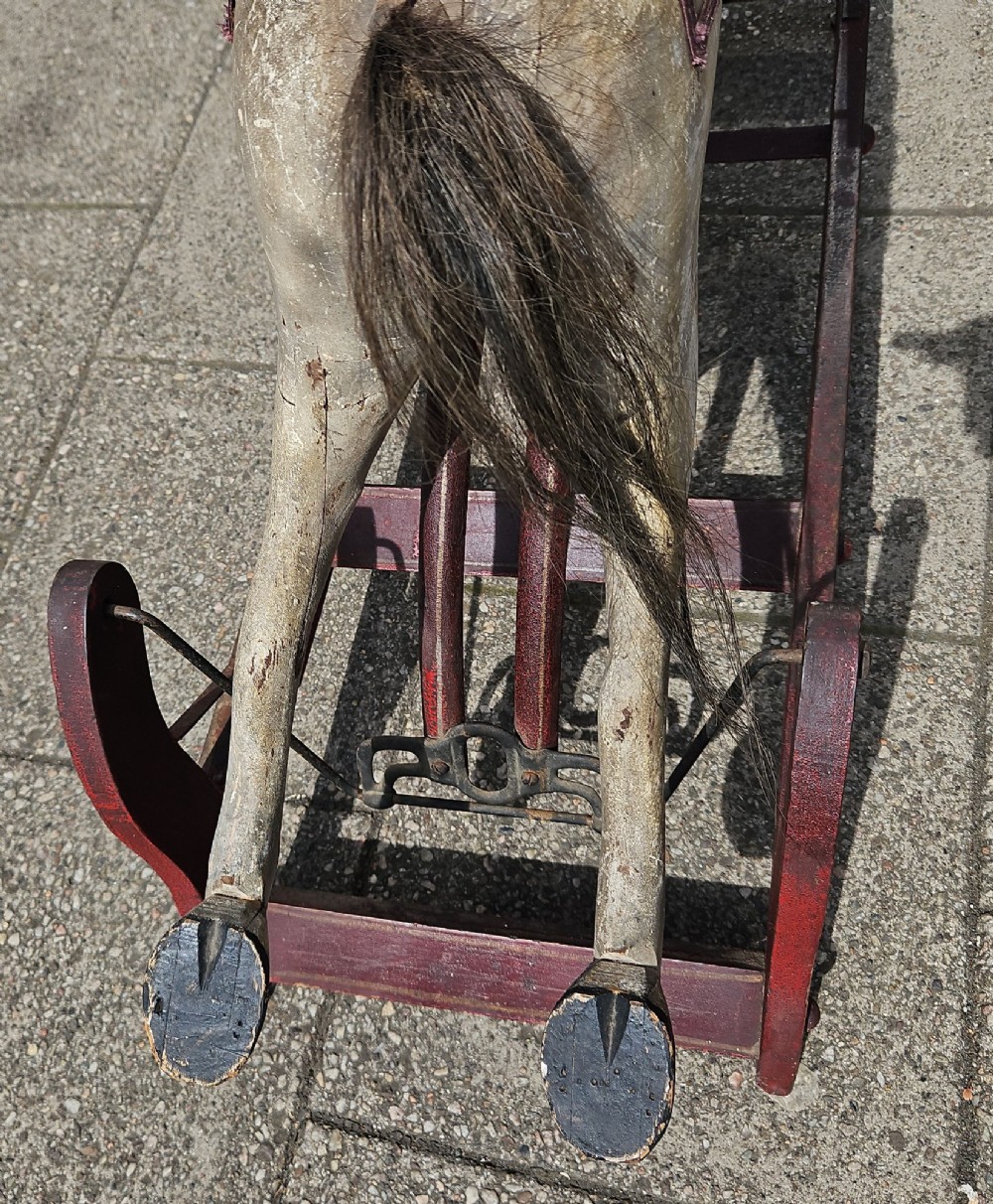 An antique carved wooden rocking horse with a grey painted finish, dark leather saddle, and black horsehair mane, mounted on a dark red glider stand. View XI
