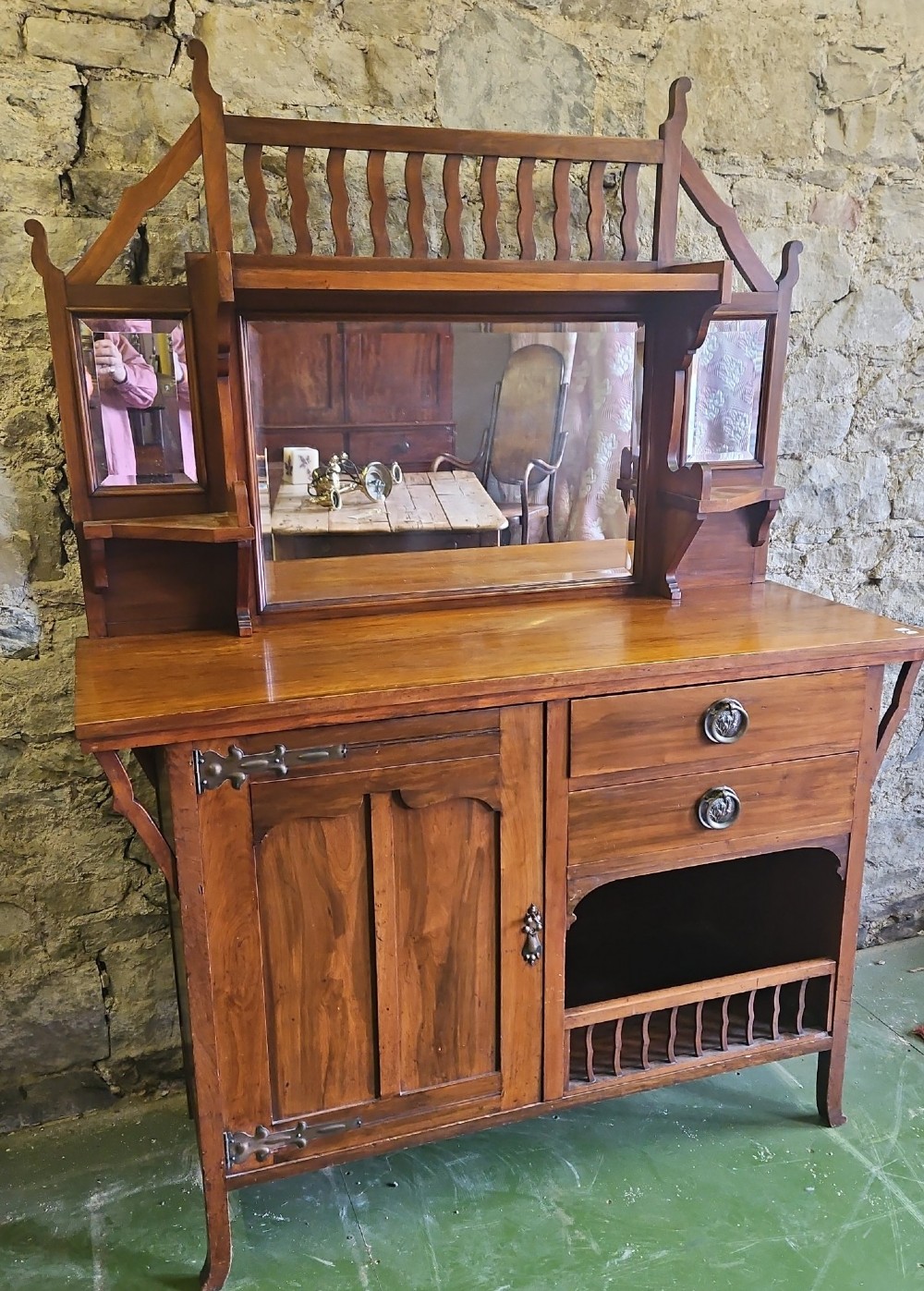 An Arts and Crafts solid wood sideboard featuring decorative iron strap hinges, a central mirror superstructure with upper spindle gallery, and lower storage drawers and cupboard.