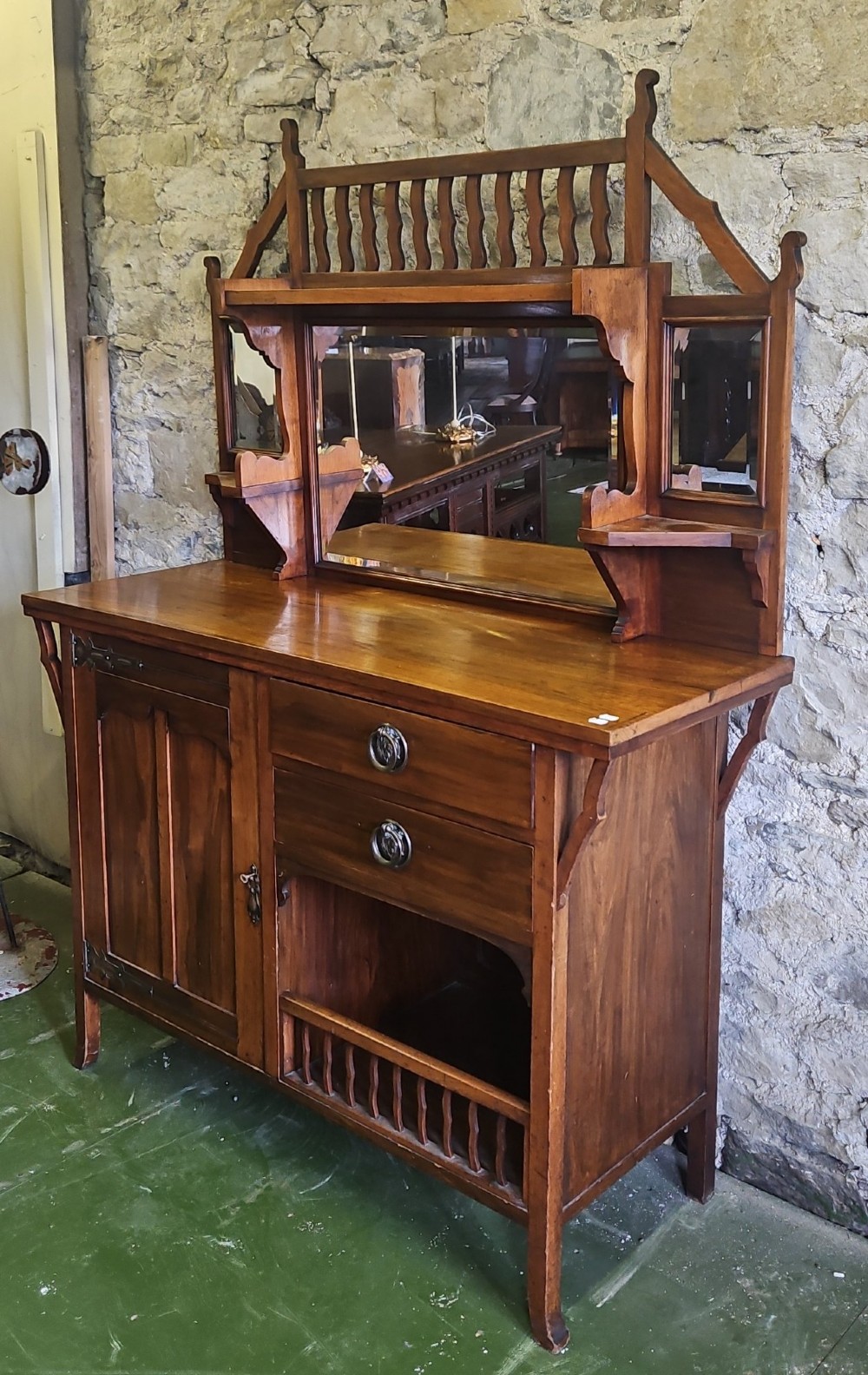 An Arts and Crafts solid wood sideboard featuring decorative iron strap hinges, a central mirror superstructure with upper spindle gallery, and lower storage drawers and cupboard. View II