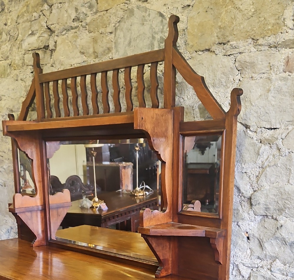 An Arts and Crafts solid wood sideboard featuring decorative iron strap hinges, a central mirror superstructure with upper spindle gallery, and lower storage drawers and cupboard. View IV