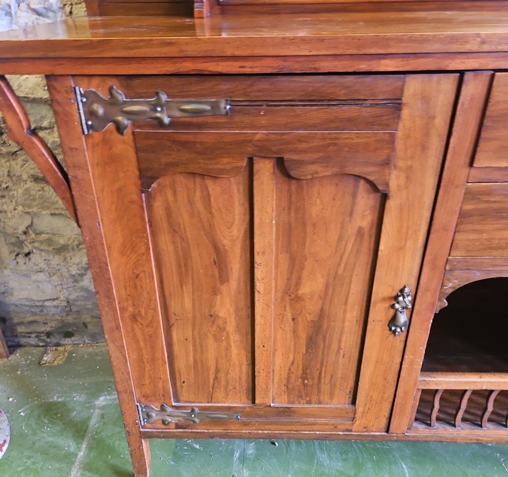 An Arts and Crafts solid wood sideboard featuring decorative iron strap hinges, a central mirror superstructure with upper spindle gallery, and lower storage drawers and cupboard. View V