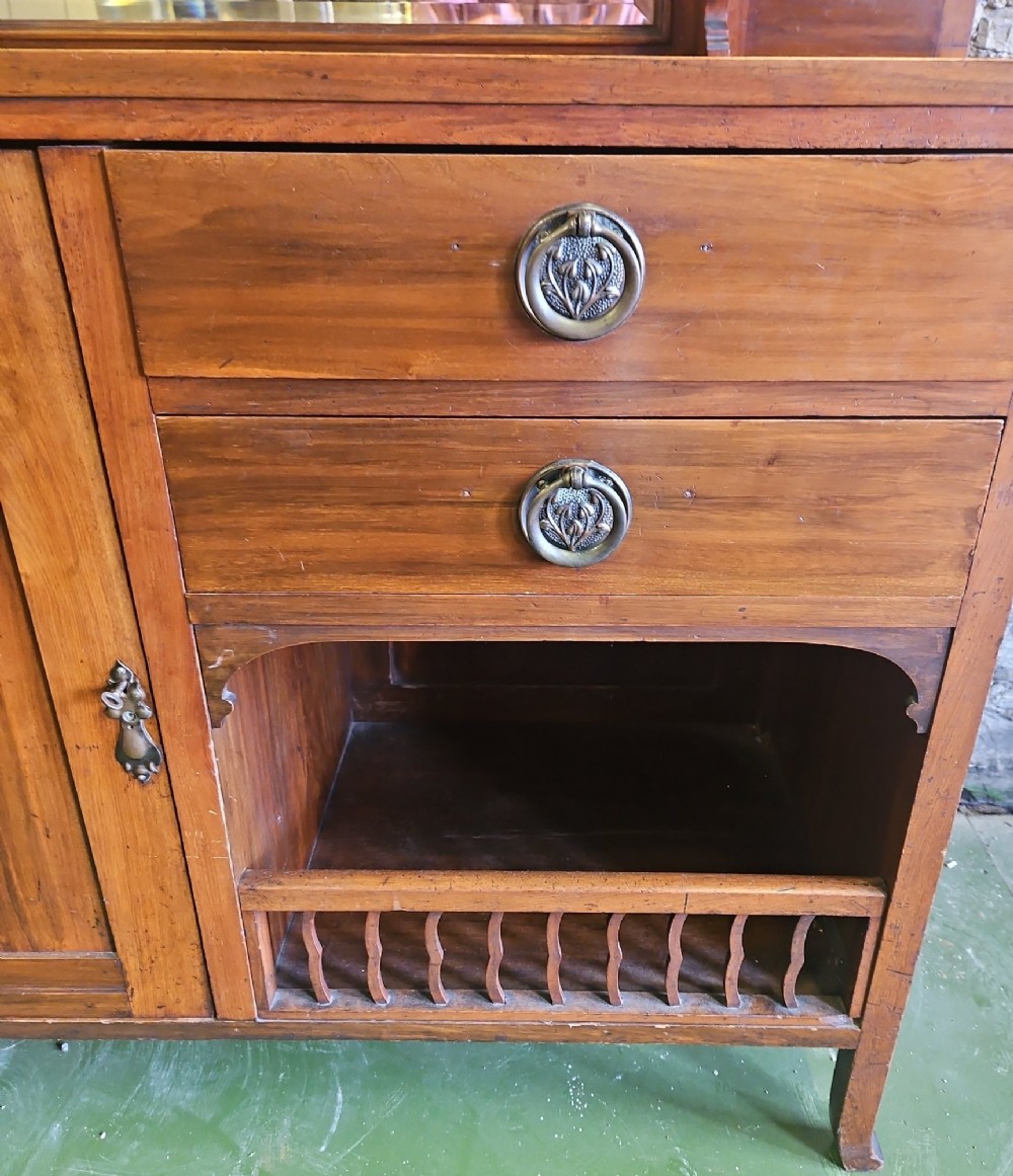 An Arts and Crafts solid wood sideboard featuring decorative iron strap hinges, a central mirror superstructure with upper spindle gallery, and lower storage drawers and cupboard. View VI