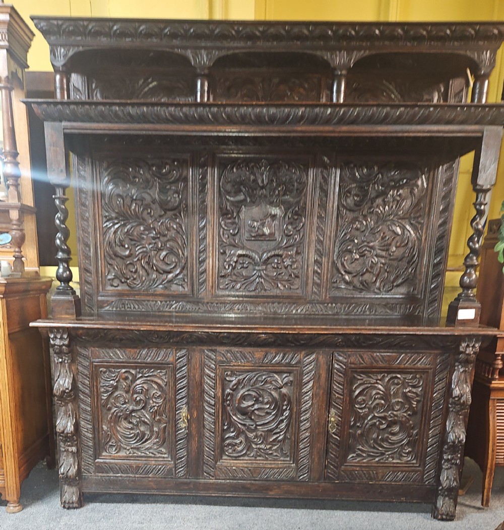 A heavily carved dark oak Jacobean style dresser featuring an open tiered upper rack supported by barley twist columns over a three-door base cupboard with carved relief panels.
