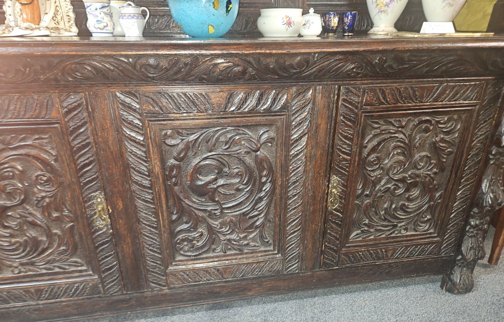 A heavily carved dark oak Jacobean style dresser featuring an open tiered upper rack supported by barley twist columns over a three-door base cupboard with carved relief panels. View VII
