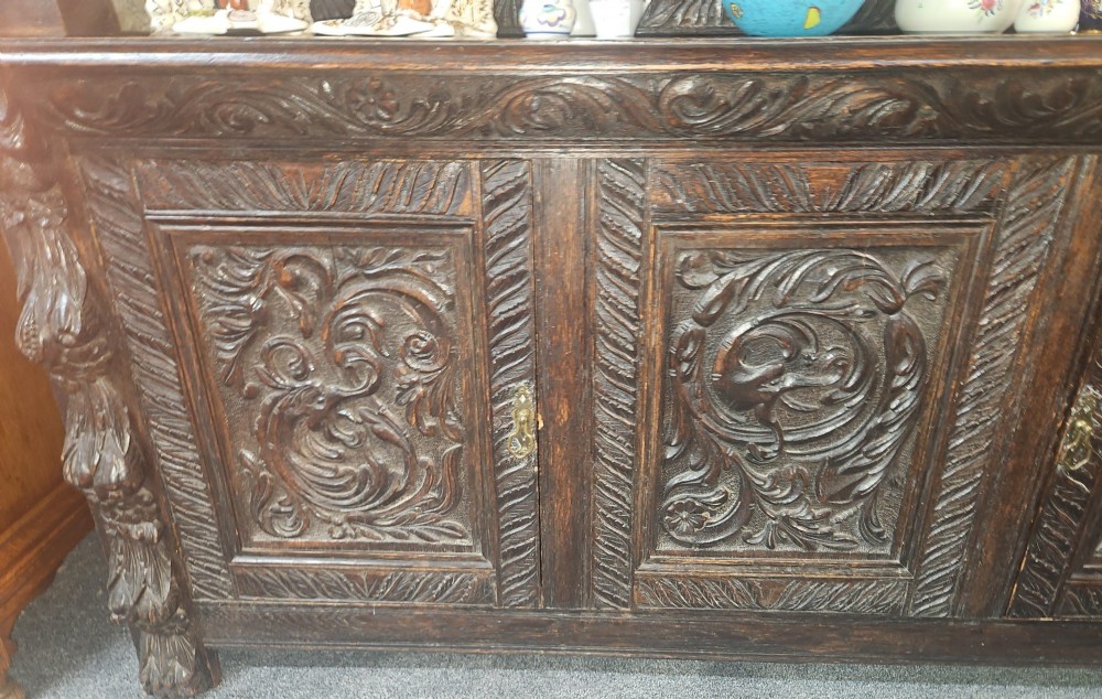 A heavily carved dark oak Jacobean style dresser featuring an open tiered upper rack supported by barley twist columns over a three-door base cupboard with carved relief panels. View VIII