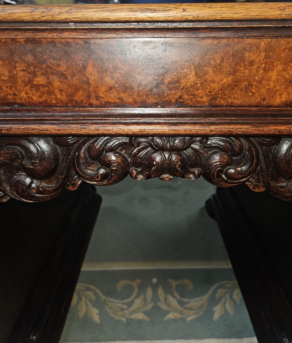 A dark carved oak pedestal desk featuring intricate relief scrollwork, carved mask motifs, geometric diamond side panels, and a flat rectangular top. View II