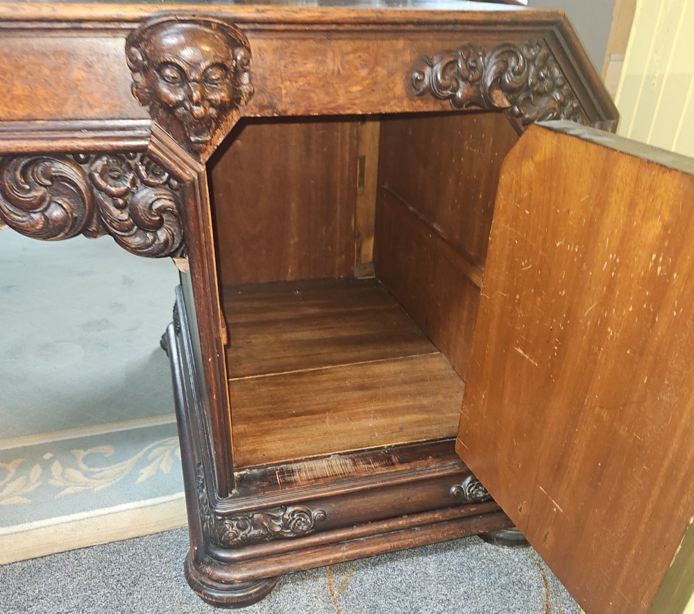 A dark carved oak pedestal desk featuring intricate relief scrollwork, carved mask motifs, geometric diamond side panels, and a flat rectangular top. View III