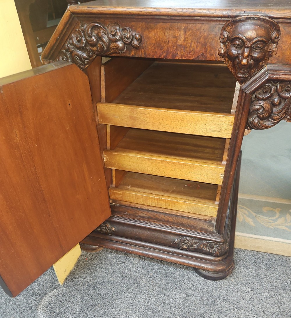 A dark carved oak pedestal desk featuring intricate relief scrollwork, carved mask motifs, geometric diamond side panels, and a flat rectangular top. View IV