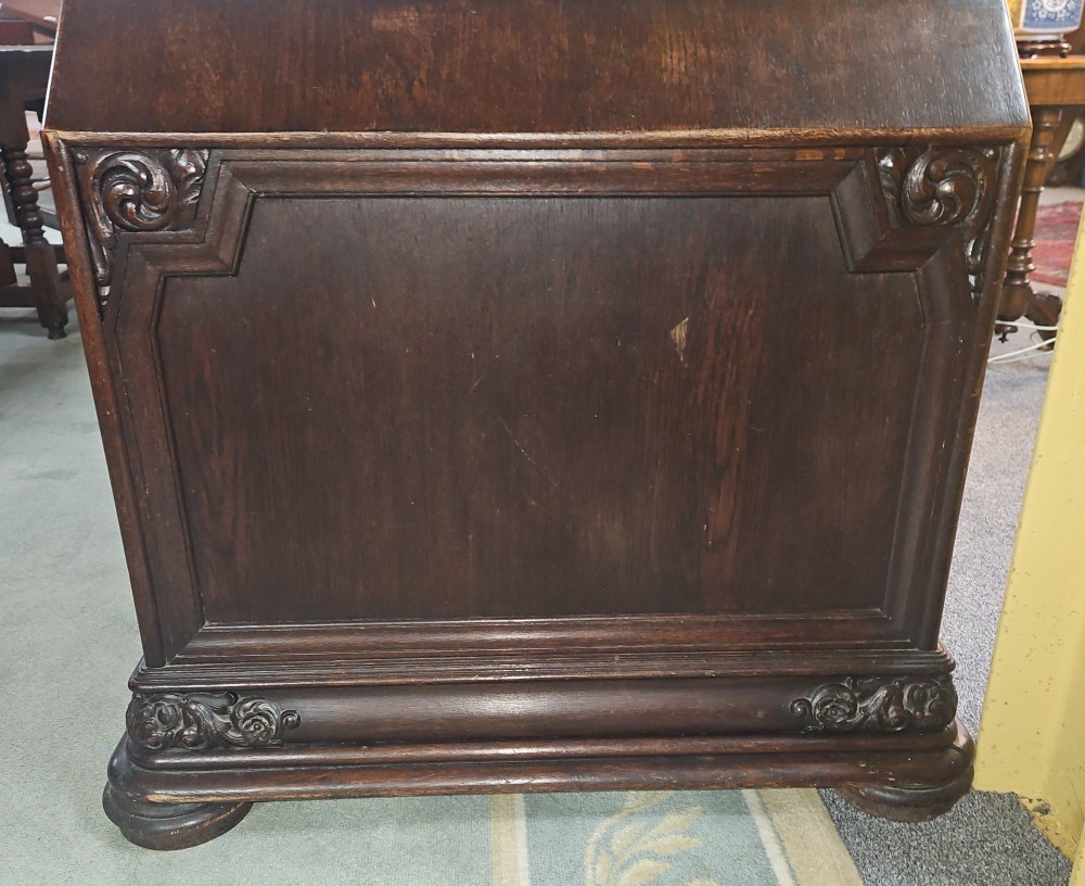 A dark carved oak pedestal desk featuring intricate relief scrollwork, carved mask motifs, geometric diamond side panels, and a flat rectangular top. View V