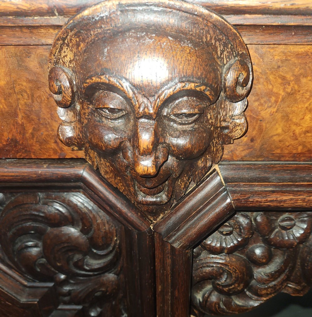 A dark carved oak pedestal desk featuring intricate relief scrollwork, carved mask motifs, geometric diamond side panels, and a flat rectangular top. View VII