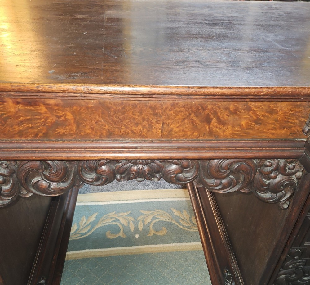 A dark carved oak pedestal desk featuring intricate relief scrollwork, carved mask motifs, geometric diamond side panels, and a flat rectangular top. View VIII