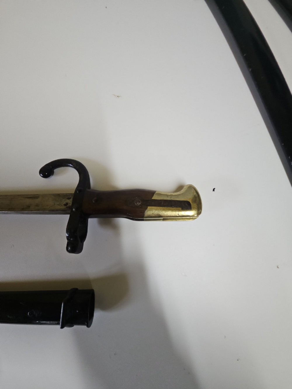 A late 19th-century French military bayonet hilt with a brass pommel, walnut handle scales, a curved steel quillon, and a metal scabbard.