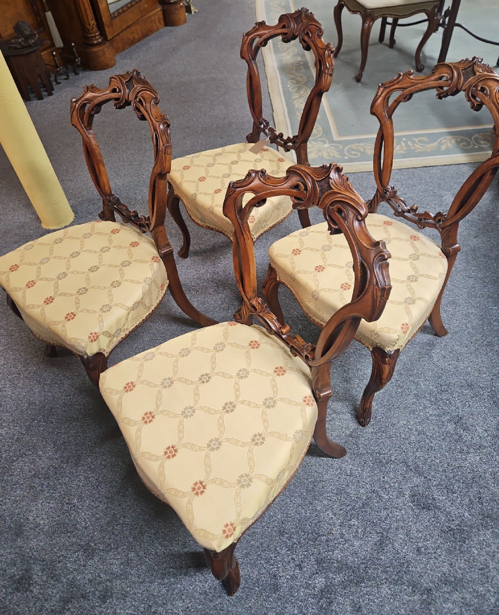 A set of four Victorian carved walnut chairs featuring intricate openwork scroll backrests, patterned cream upholstery, and cabriole legs.