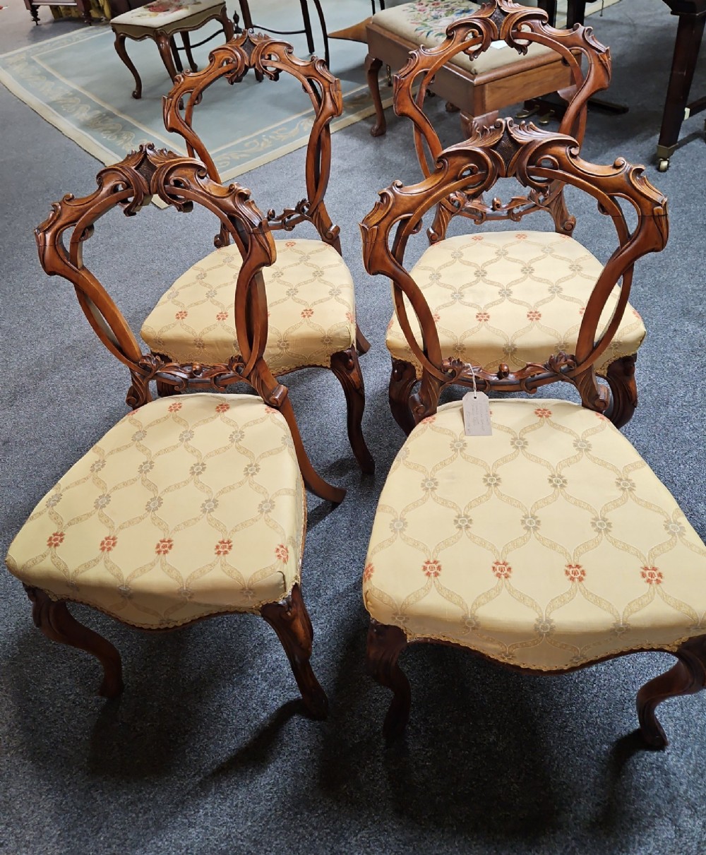 A set of four Victorian carved walnut chairs featuring intricate openwork scroll backrests, patterned cream upholstery, and cabriole legs. View II