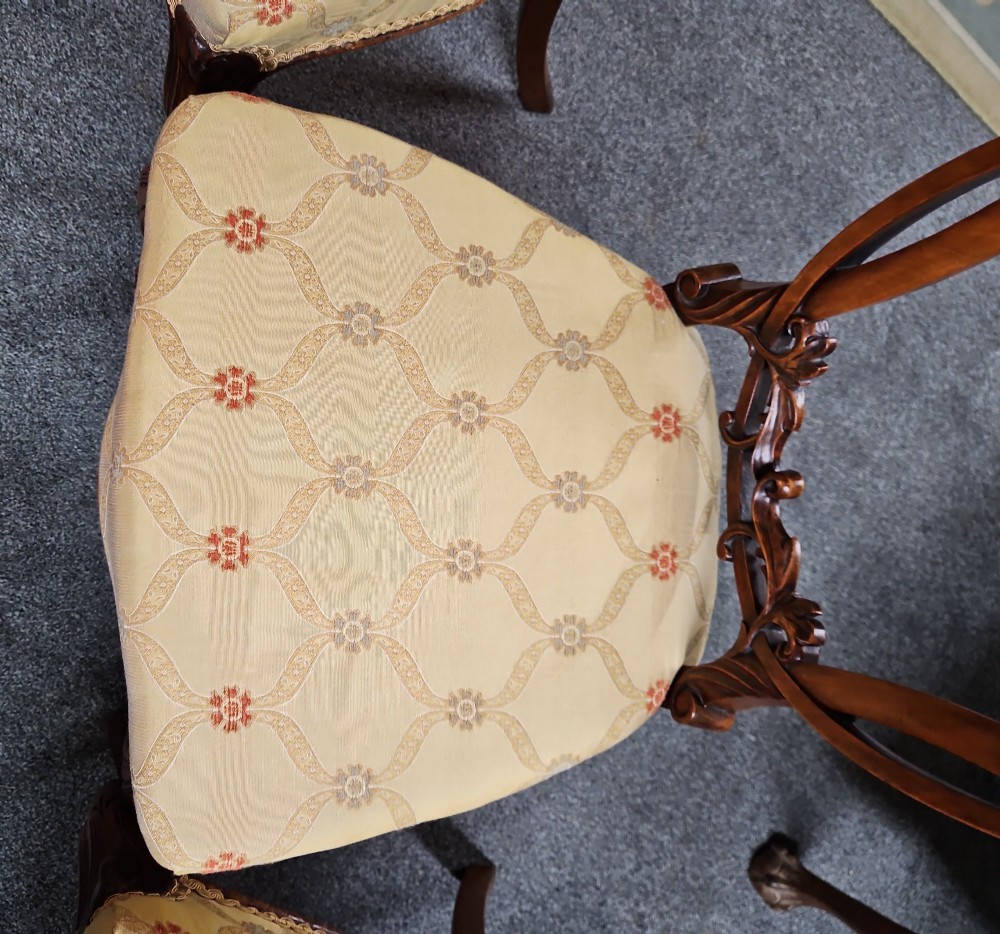 A set of four Victorian carved walnut chairs featuring intricate openwork scroll backrests, patterned cream upholstery, and cabriole legs. View III