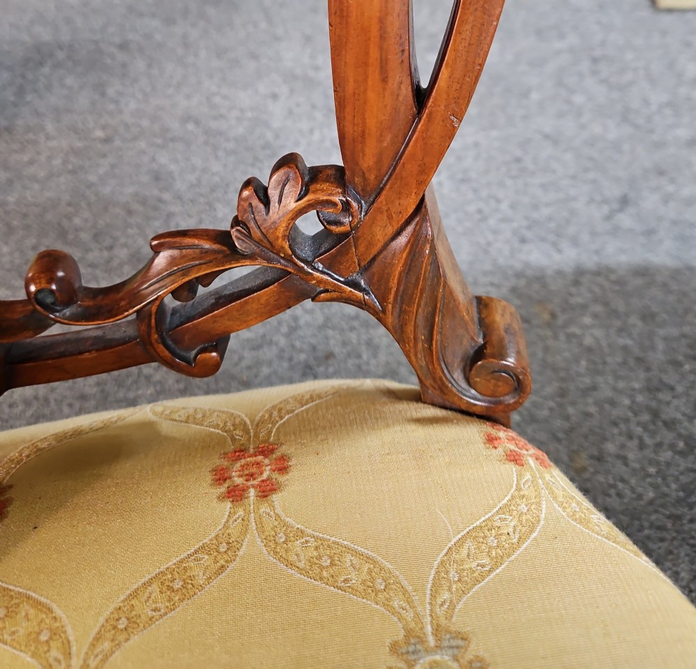 A set of four Victorian carved walnut chairs featuring intricate openwork scroll backrests, patterned cream upholstery, and cabriole legs. View IV