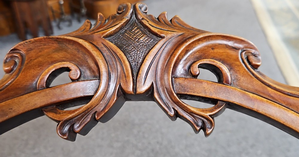 A set of four Victorian carved walnut chairs featuring intricate openwork scroll backrests, patterned cream upholstery, and cabriole legs. View VI