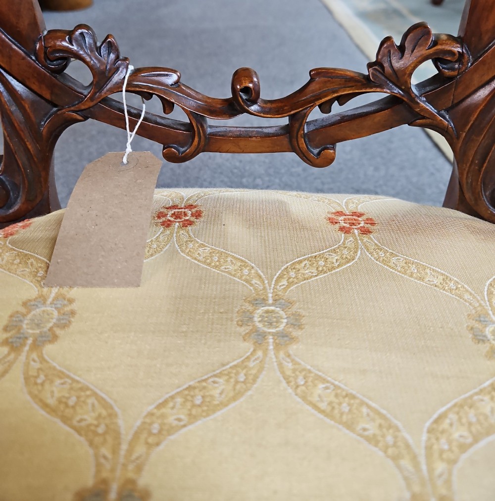 A set of four Victorian carved walnut chairs featuring intricate openwork scroll backrests, patterned cream upholstery, and cabriole legs. View VII