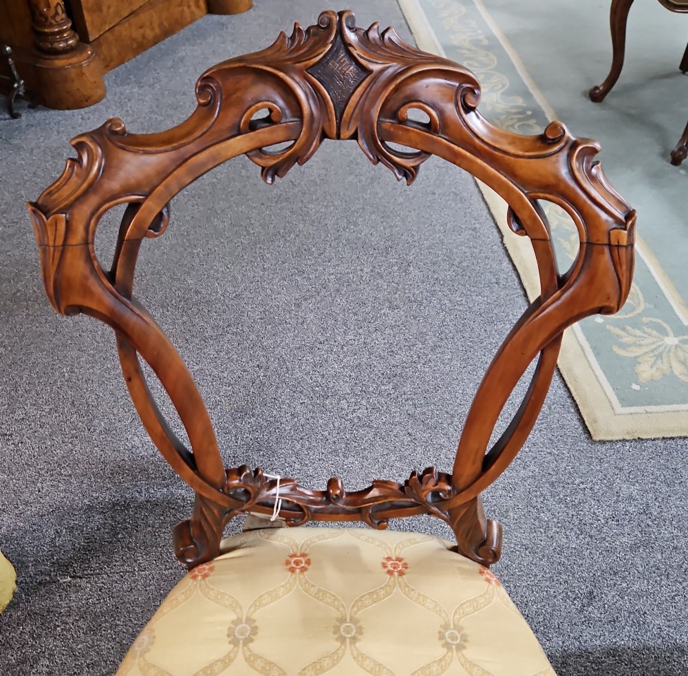 A set of four Victorian carved walnut chairs featuring intricate openwork scroll backrests, patterned cream upholstery, and cabriole legs. View IX