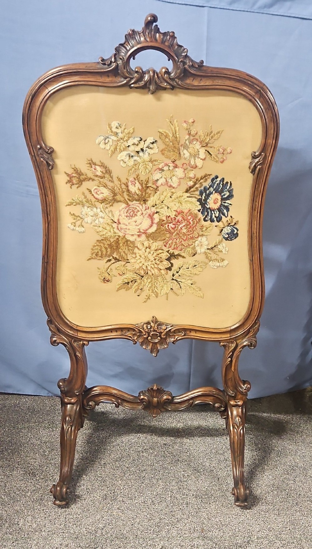 A Victorian carved walnut fire screen featuring an ornate cresting frame supported by cabriole legs, encasing a floral needlepoint textile panel.