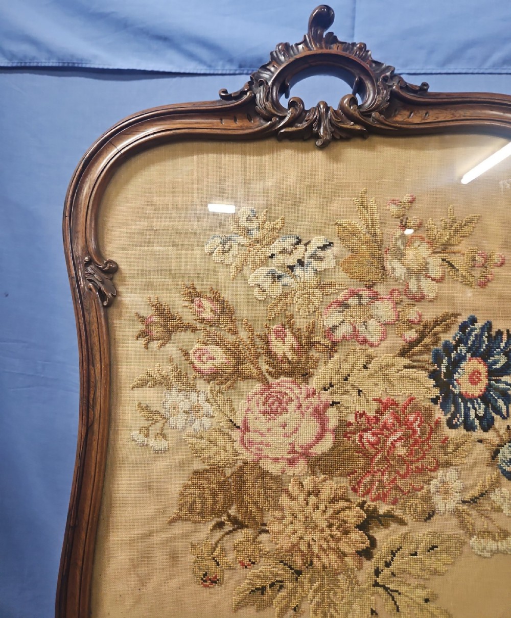 A Victorian carved walnut fire screen featuring an ornate cresting frame supported by cabriole legs, encasing a floral needlepoint textile panel. View V