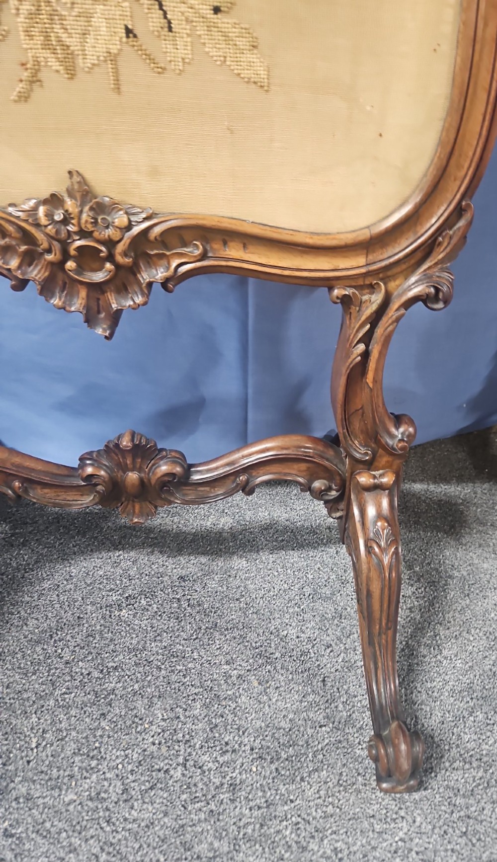 A Victorian carved walnut fire screen featuring an ornate cresting frame supported by cabriole legs, encasing a floral needlepoint textile panel. View VI