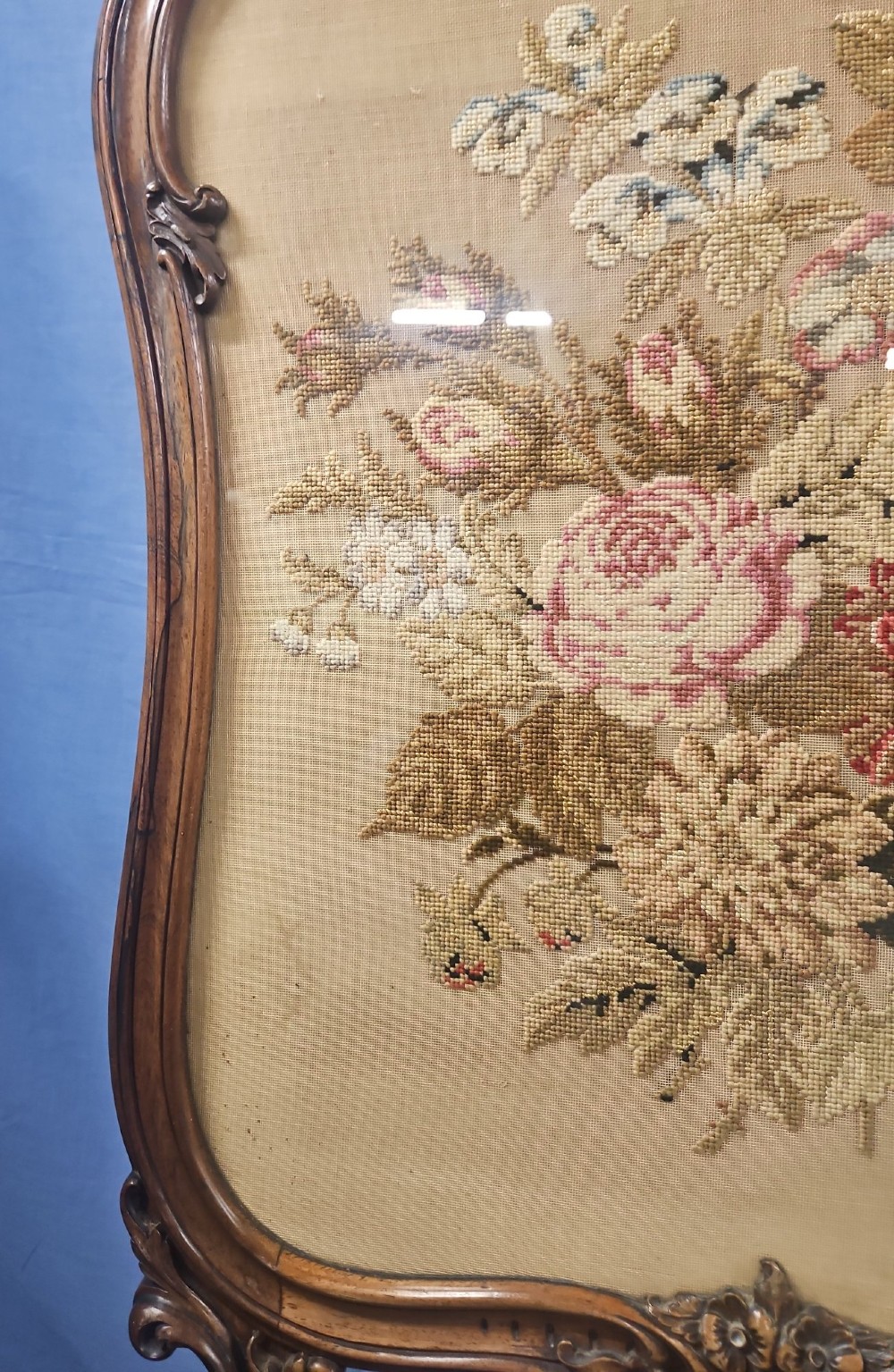A Victorian carved walnut fire screen featuring an ornate cresting frame supported by cabriole legs, encasing a floral needlepoint textile panel. View VII