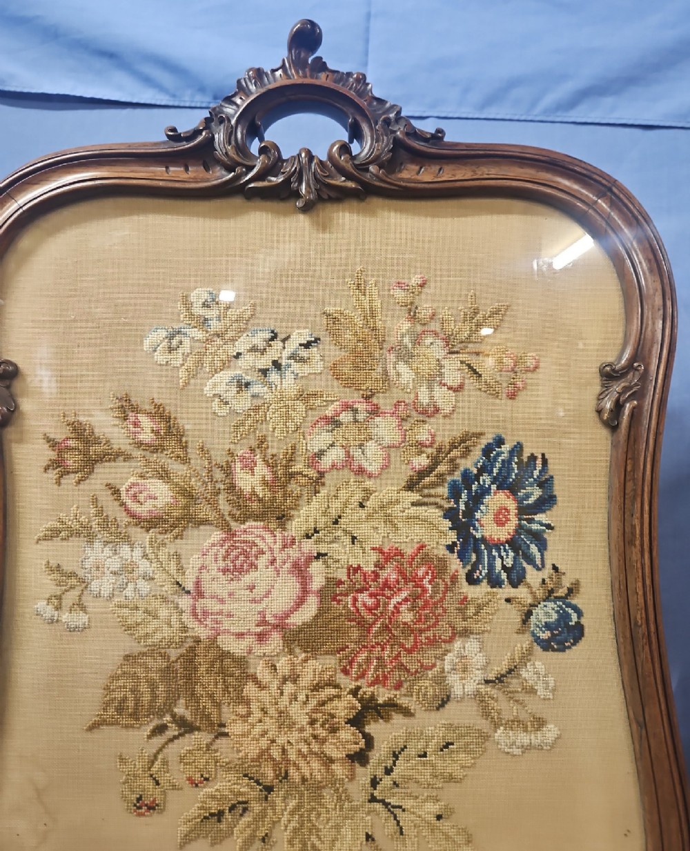 A Victorian carved walnut fire screen featuring an ornate cresting frame supported by cabriole legs, encasing a floral needlepoint textile panel. View IX